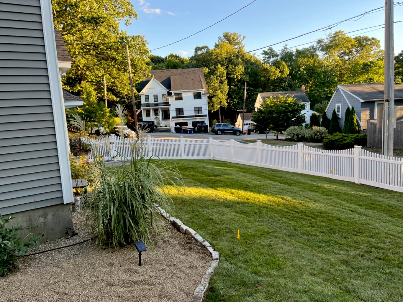 A grassy front yard with a white picket fence and suburban houses in the background.
