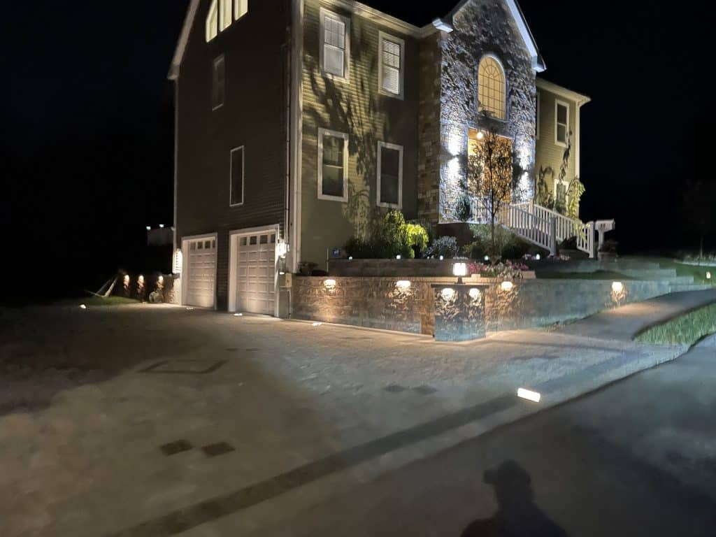 Illuminated house exterior with garage and lit pathway at night.