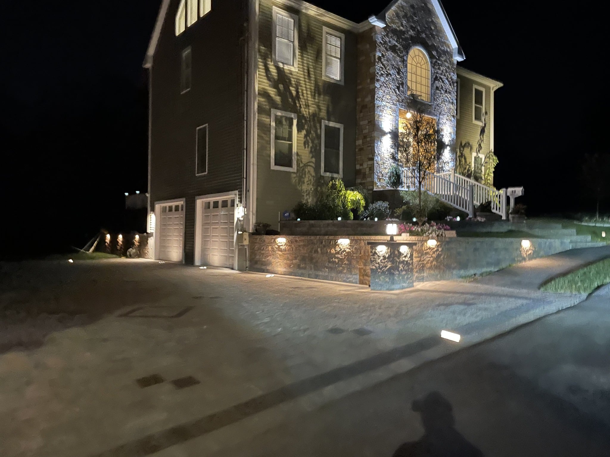 Illuminated house exterior with garage and lit pathway at night.