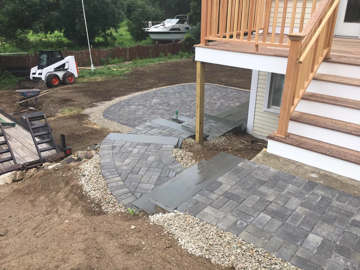 Newly installed stone patio and stairs in front of a house under construction, with a small excavator nearby.